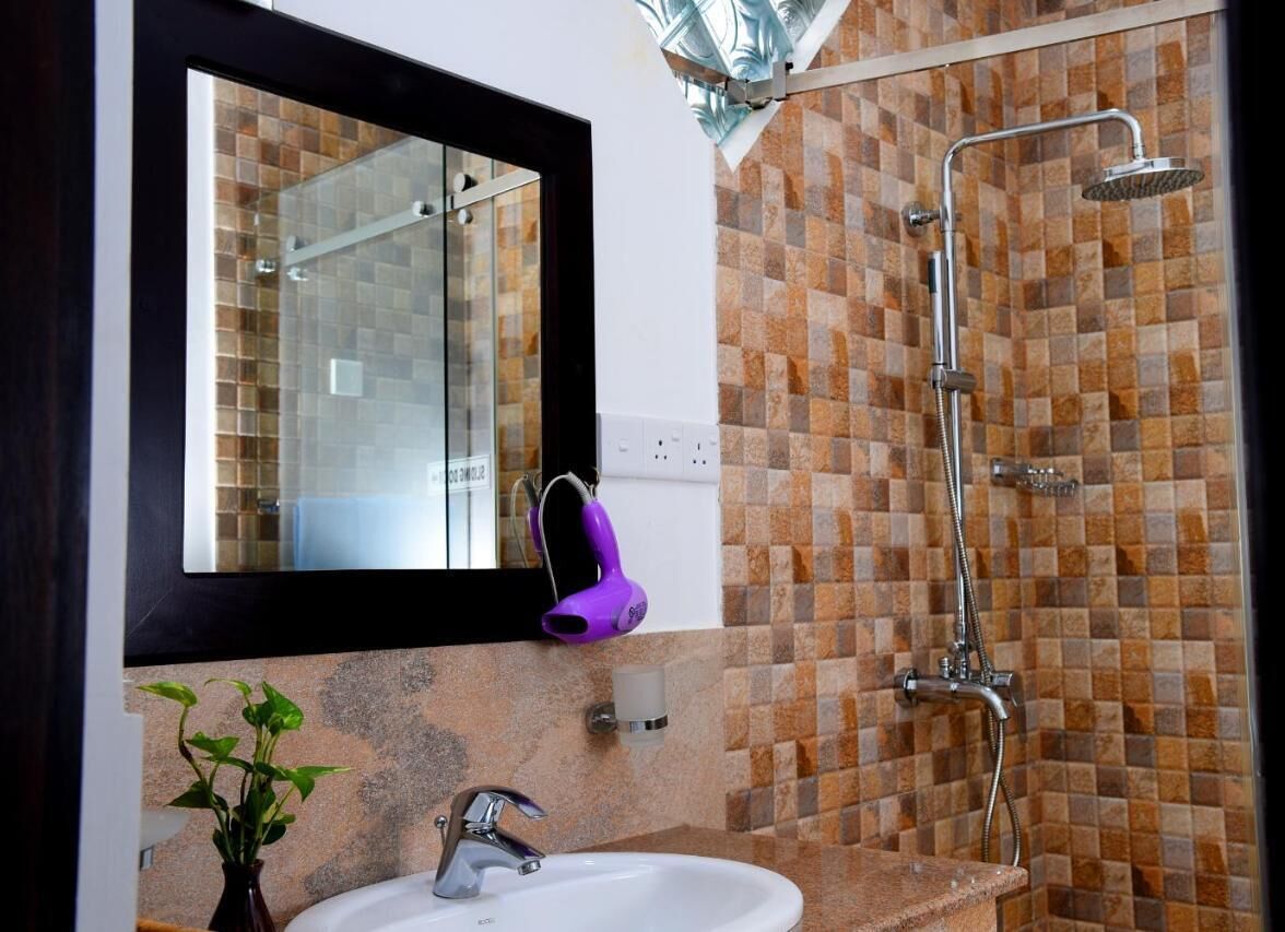Een badkamer met een douchecabine van glas, een wit wastafeltje en een spiegel met een zwarte lijst.