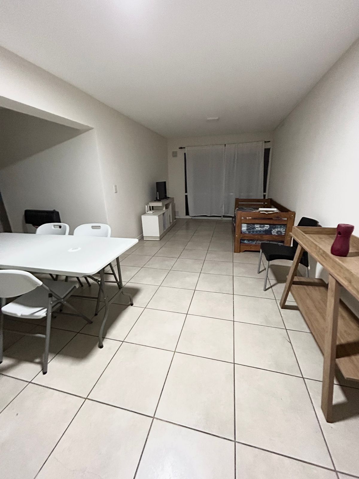 Ein kleines Zimmer mit einem weißen Tisch und Stühlen, einem kleinen Schrank und einer hölzernen Bank.