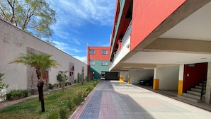 A multi-story parking garage with a red and white facade, a clear sky, and a pathway leading to the entrance. - Confortable departamento en Mendoza (Mendoza)