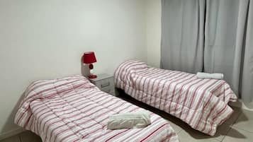 A room with two beds, a nightstand, a lamp, and a window with curtains.