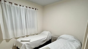 A small, clean room with two single beds, a window with white curtains, and a ceiling light. - Confortable departamento en Mendoza (Mendoza)