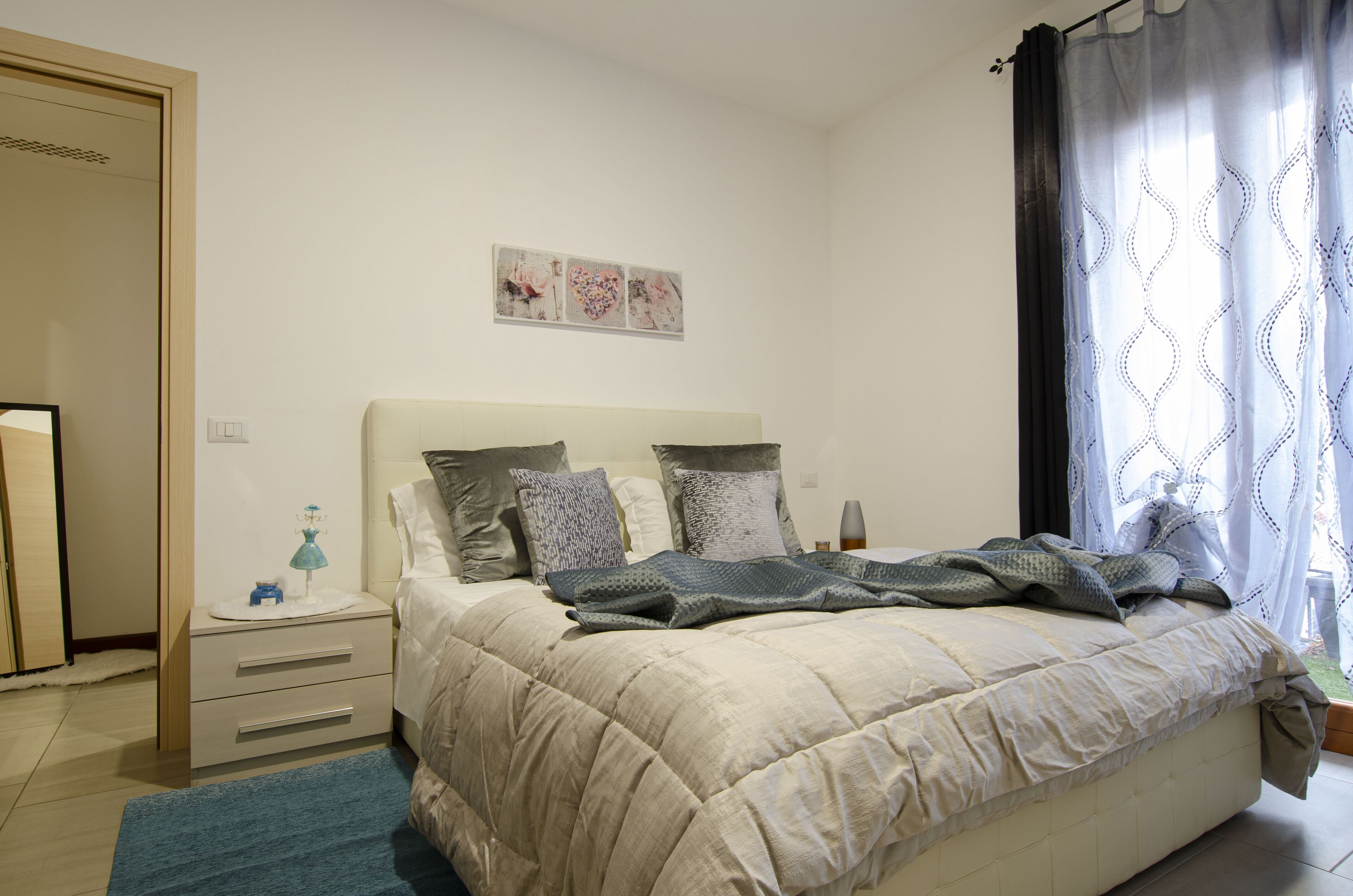 A bedroom with a bed, nightstands, a dresser, and a window with curtains.