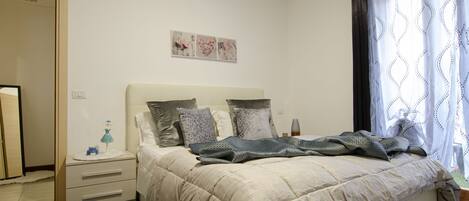 A bedroom with a bed, nightstands, a dresser, and a window with curtains.