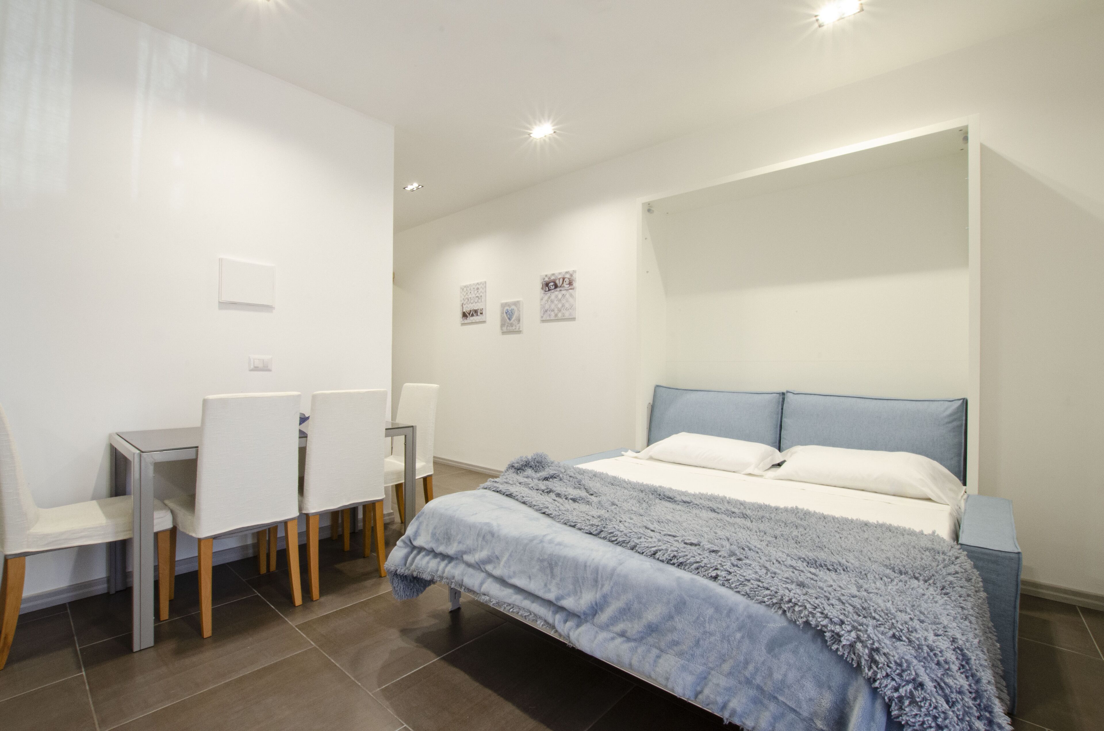 Een slaapkamer met een bed, nachtkastjes, een bureau met stoelen en een wandlamp.