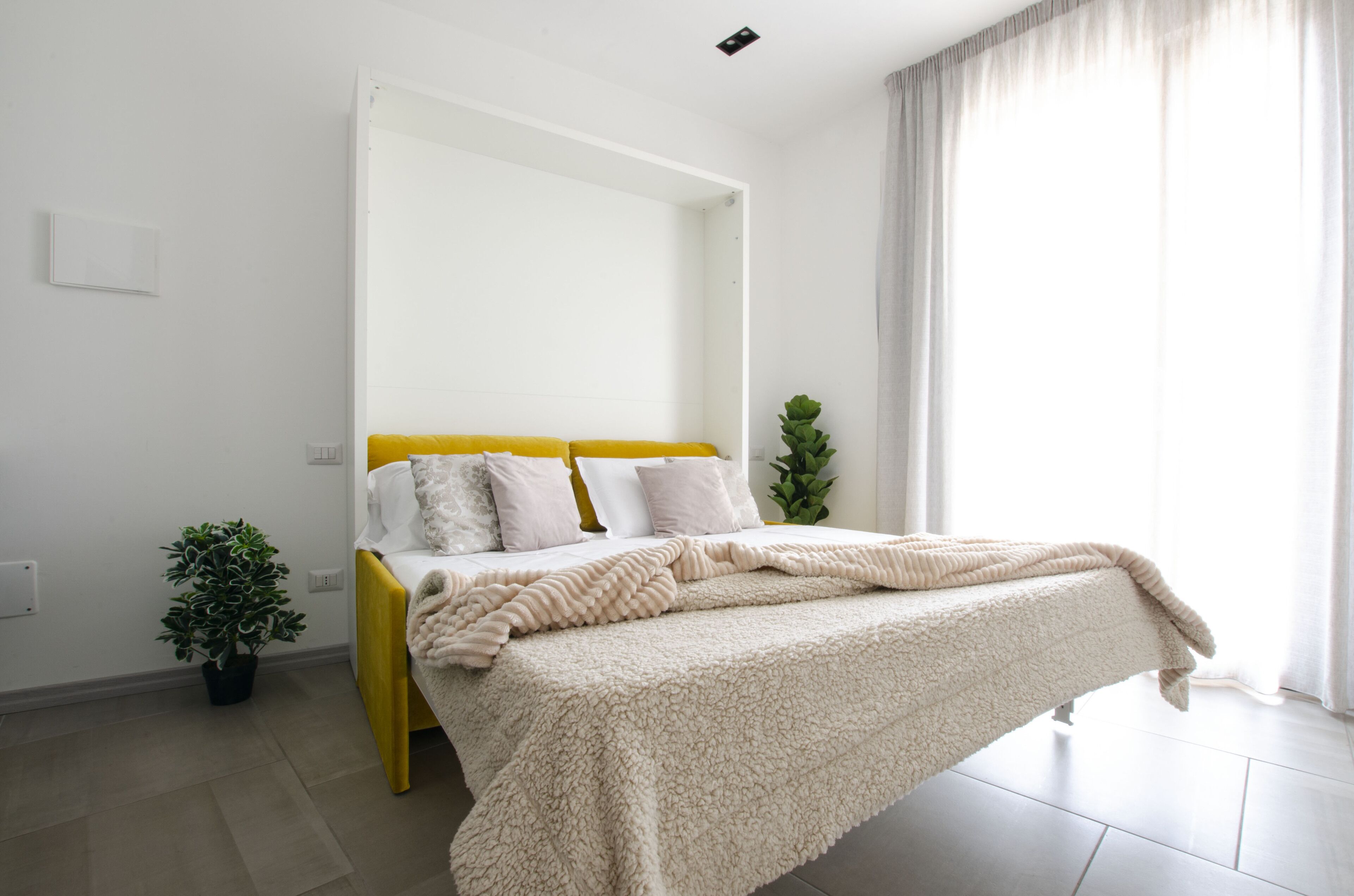 Una camera da letto con un letto, una pianta sul comodino e una finestra con tende.