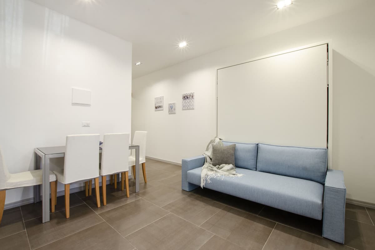 Una habitación moderna con una mesa de comedor y sillas, un sofá azul y una pizarra en la pared.