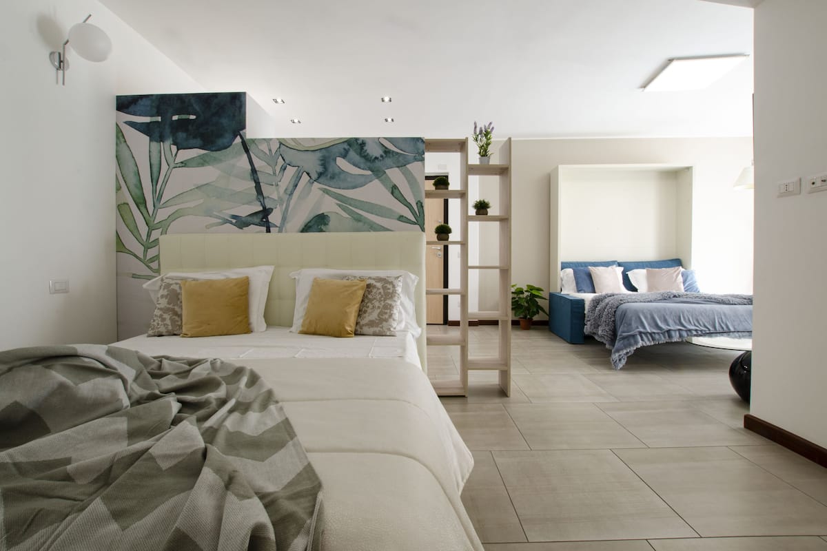 Un dormitorio moderno con una cama grande, una cama más pequeña, una escalera y un estante con plantas.
