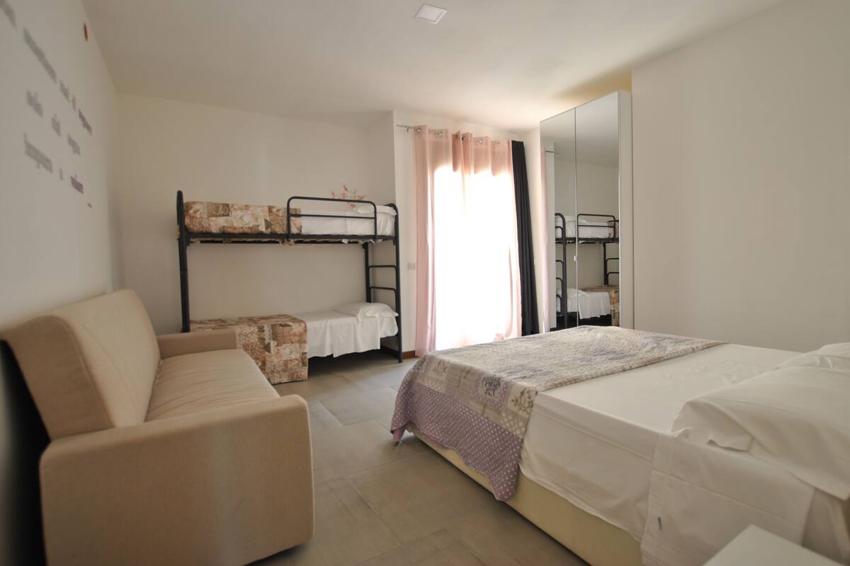 Una habitación con literas, un sofá, un espejo y una ventana con cortinas.