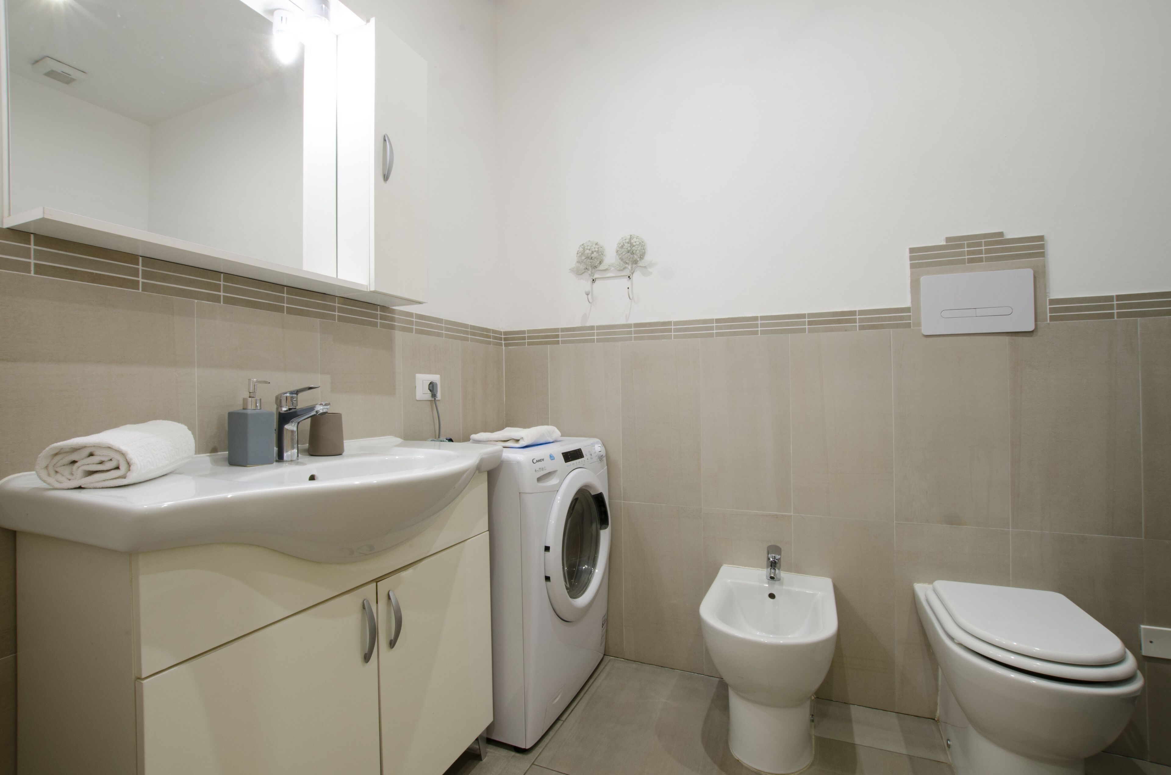 A modern bathroom with a sink, washing machine, bidet, and toilet.
