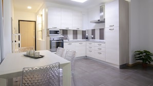 Una cocina moderna con armarios blancos, horno integrado y microondas. Hay una mesa de comedor con sillas y una bandeja de velas.