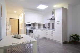 A modern kitchen with white cabinetry, a built-in oven, and a microwave. There is a dining table with chairs and a tray of candles.
