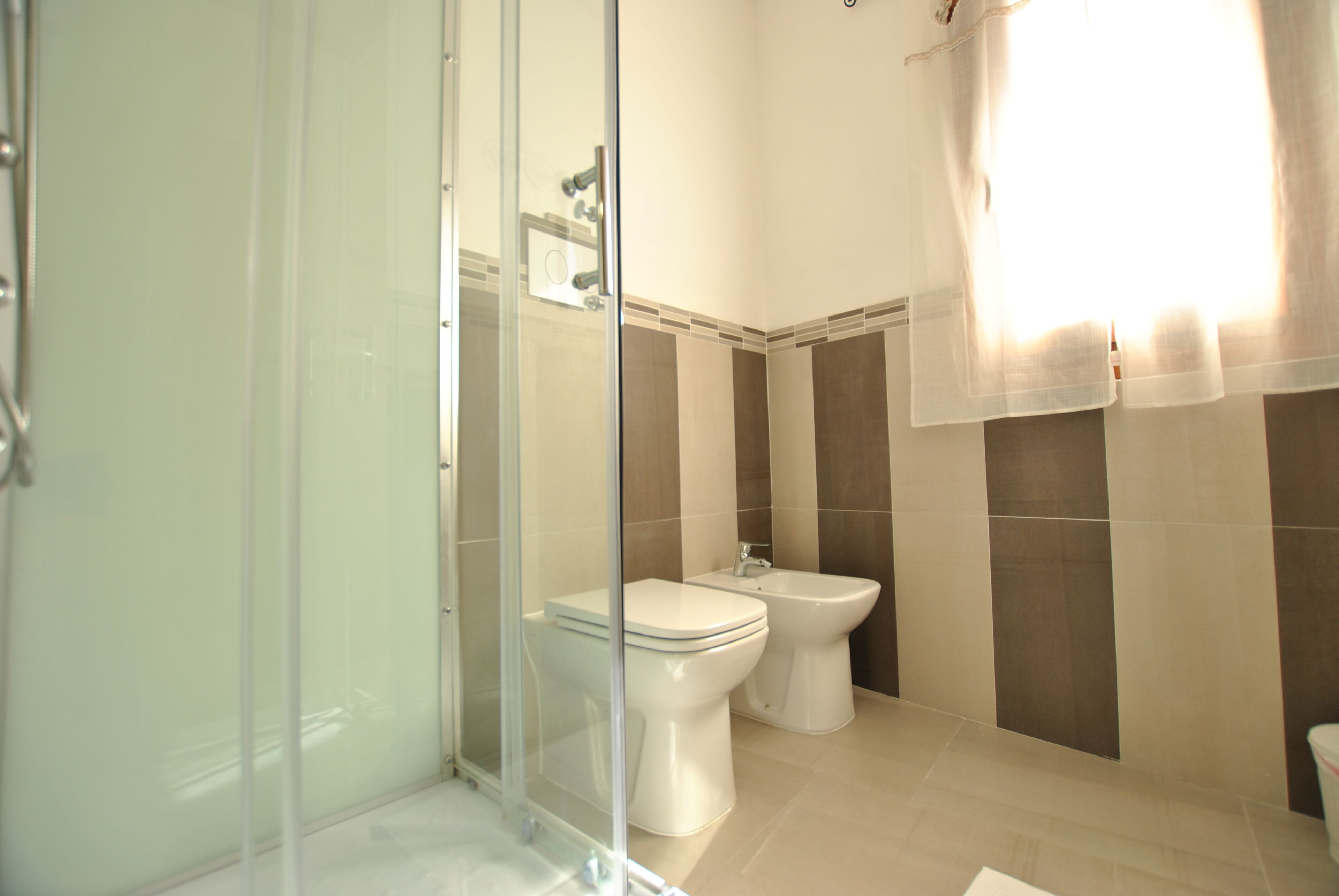 A modern bathroom with a glass shower enclosure, a toilet, and a bidet.