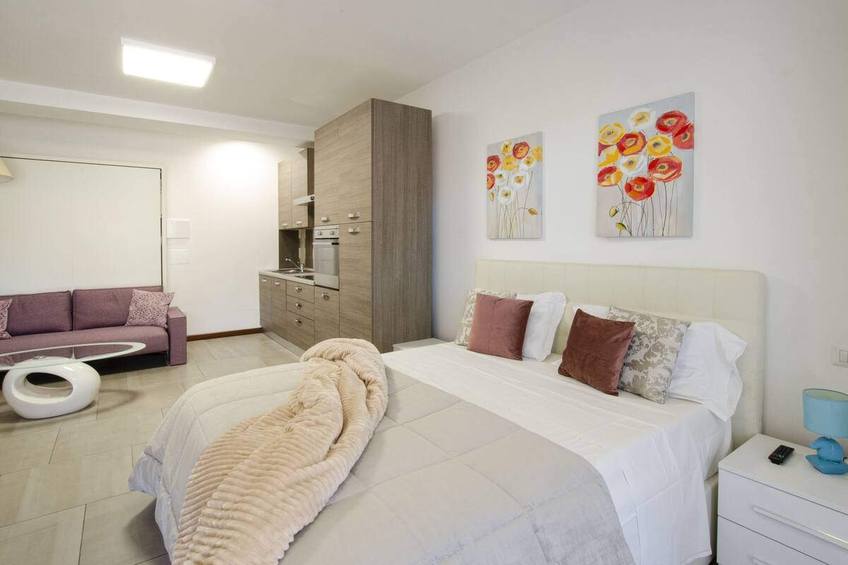 Un dormitorio moderno con una cama grande, un sofá, una mesa de comedor y una zona de cocina.