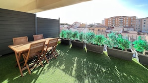Una terraza en la azotea con mesa y sillas de madera, rodeada de plantas en macetas y vistas panorámicas de la ciudad.