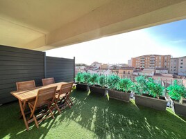Una terraza en la azotea con mesa y sillas de madera, rodeada de plantas en macetas y vistas panorámicas de la ciudad.