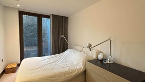 A modern bedroom with a large bed, a bedside table with a lamp, and a view through a window. - Stylish & Modern 1BD Flat - Chancery Lane! (London)