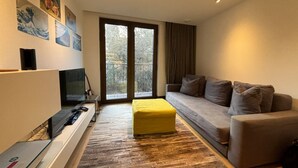 A modern living room with a sofa, a yellow ottoman, a flat-screen TV, and artwork on the wall. - Stylish & Modern 1BD Flat - Chancery Lane! (London)