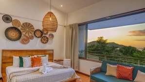 A bedroom with a wooden bed, a green sofa, and a large window with a view of greenery and hills. - Few Steps to Beach Private Pool and Jacuzzi (Sardinal)