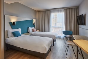 A hotel room with two beds, a desk, a chair, a TV, and a large window with curtains. - Aparthotel Adagio Heidelberg (Heidelberg)