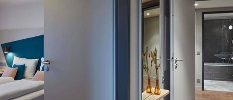 Habitación de hotel moderna con cama, mesita de noche, espejo y vista al baño.