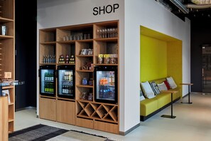 A shop area with shelves stocked with various items, a seating area with cushions, and a refrigerator with beverages. - Aparthotel Adagio Heidelberg (Heidelberg)