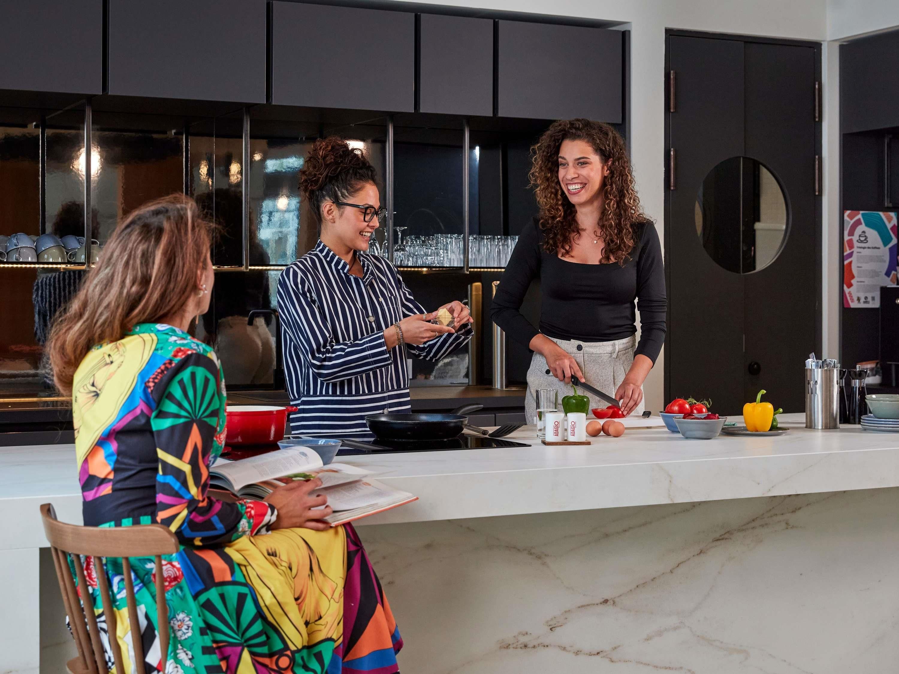 A modern kitchen with a marble countertop, a person preparing food, and another person reading a book.