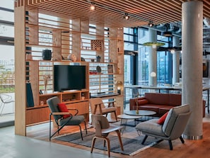 A modern lounge area with a large TV, wooden shelving, seating, and large windows. - Aparthotel Adagio Heidelberg (Heidelberg)