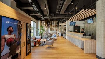 Een moderne receptiebalie met een houten toonbank, een zithoek met stoelen en tafels, en een grote poster aan de wand.