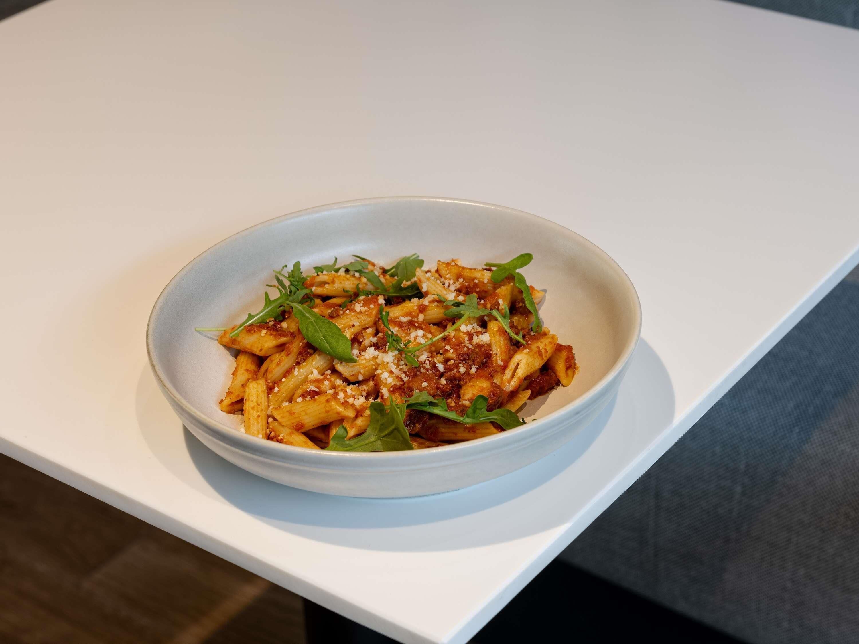 A bowl of pasta with a garnish on a white table.