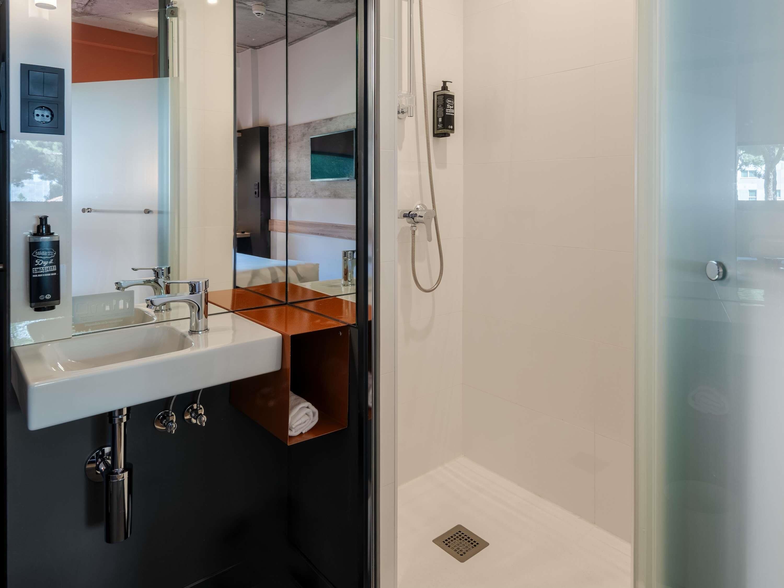 Ein modernes Badezimmer mit einer Duschkabine, einem Waschbecken mit Spiegel und einem Handtuchhalter.