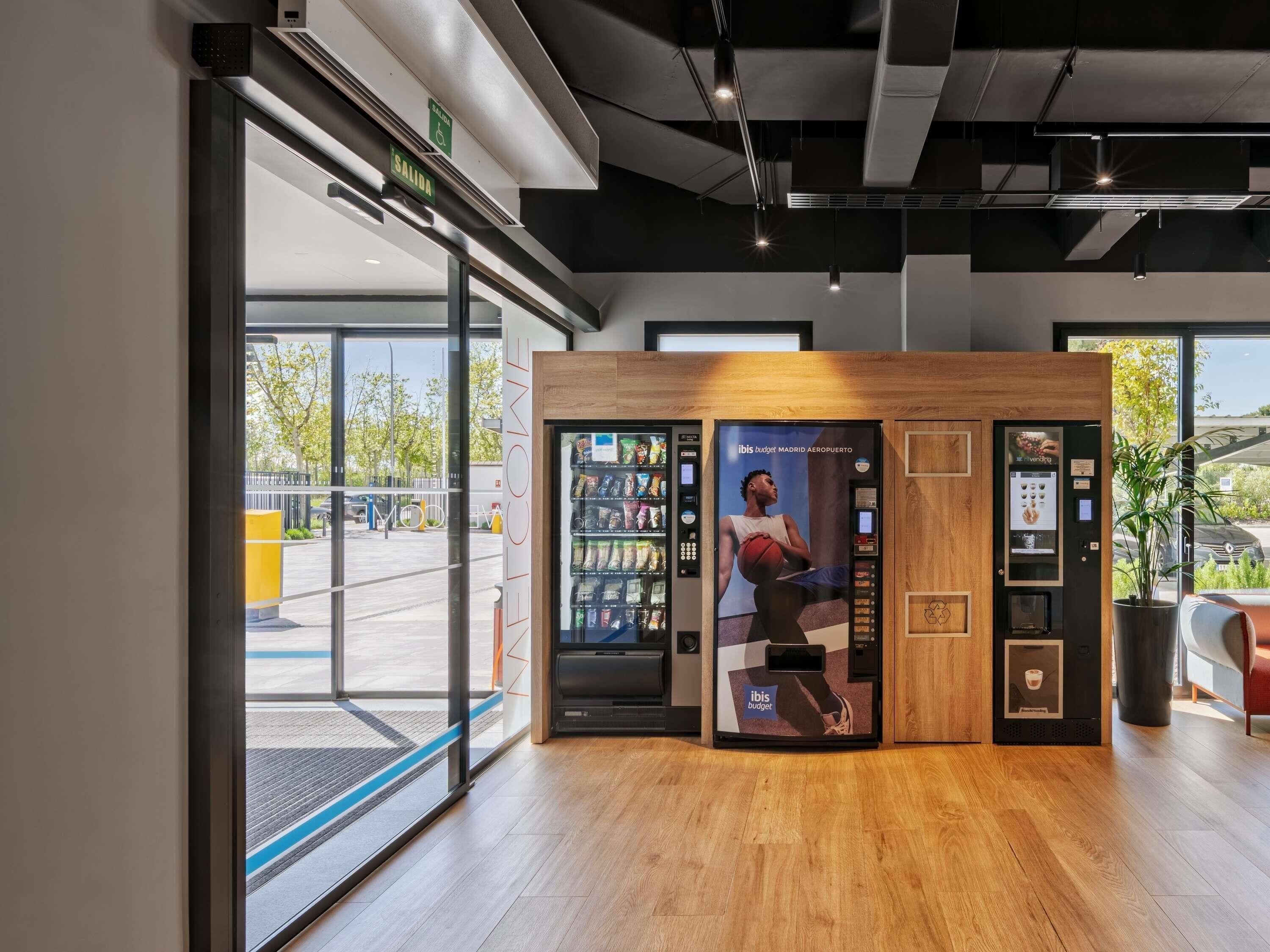 Un interior moderno con una máquina expendedora, una barra de madera y una puerta de cristal que da al exterior.