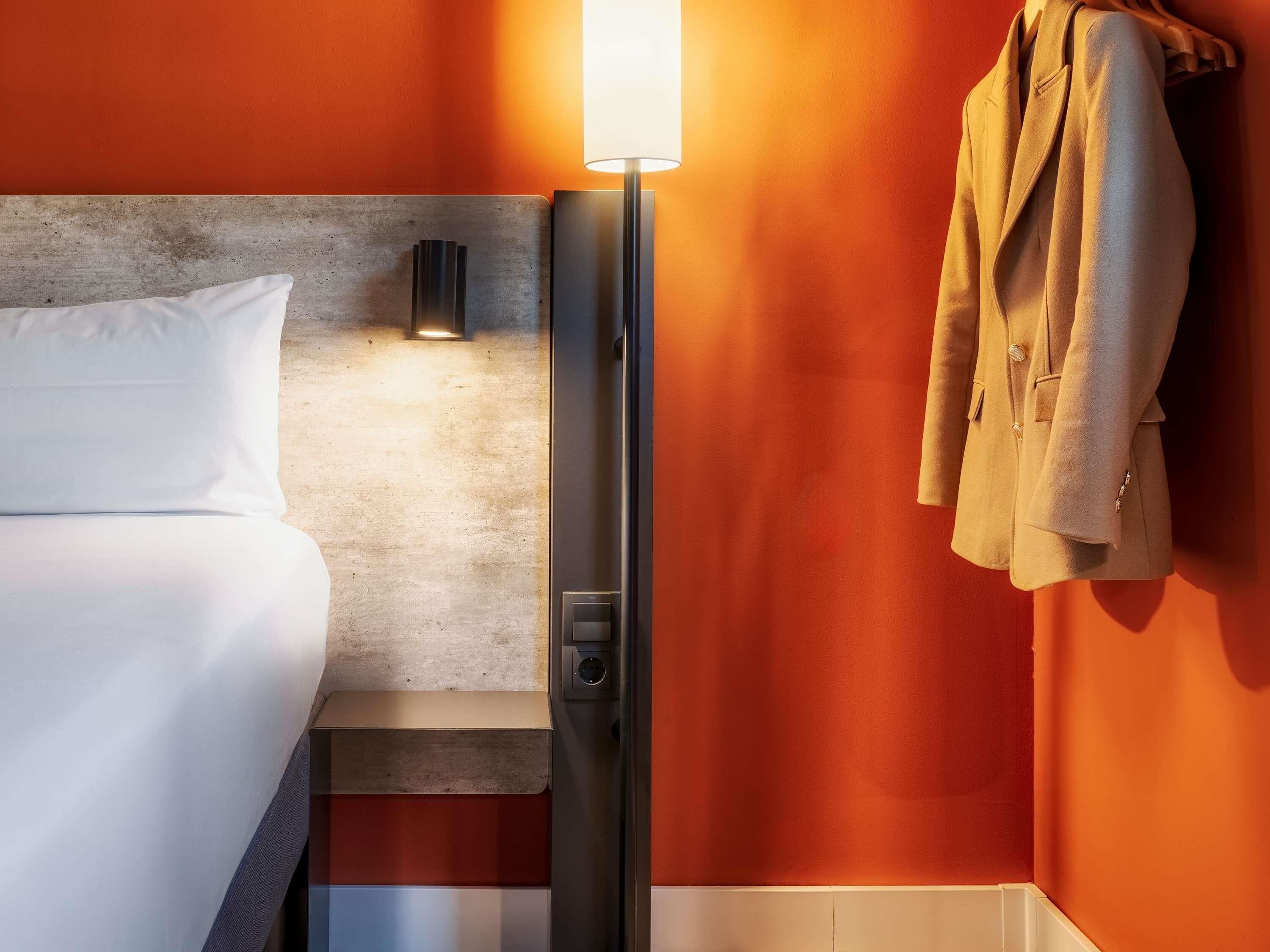 A hotel room with a bed, a nightstand, a lamp, and a coat rack.