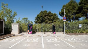 Un área de estacionamiento con estaciones de carga para vehículos eléctricos, espacios de estacionamiento delimitados y un cartel de prohibido estacionar.