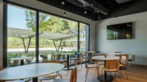 A modern indoor dining area with large windows, wooden tables, and chairs.