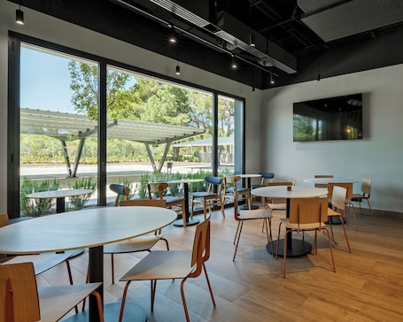 A modern indoor dining area with large windows, wooden tables, and chairs.