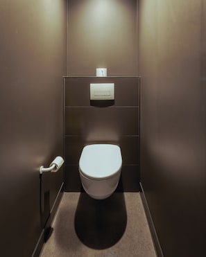 Un baño moderno con inodoro blanco, un secador de manos y dispensador de toallas de papel en la pared.