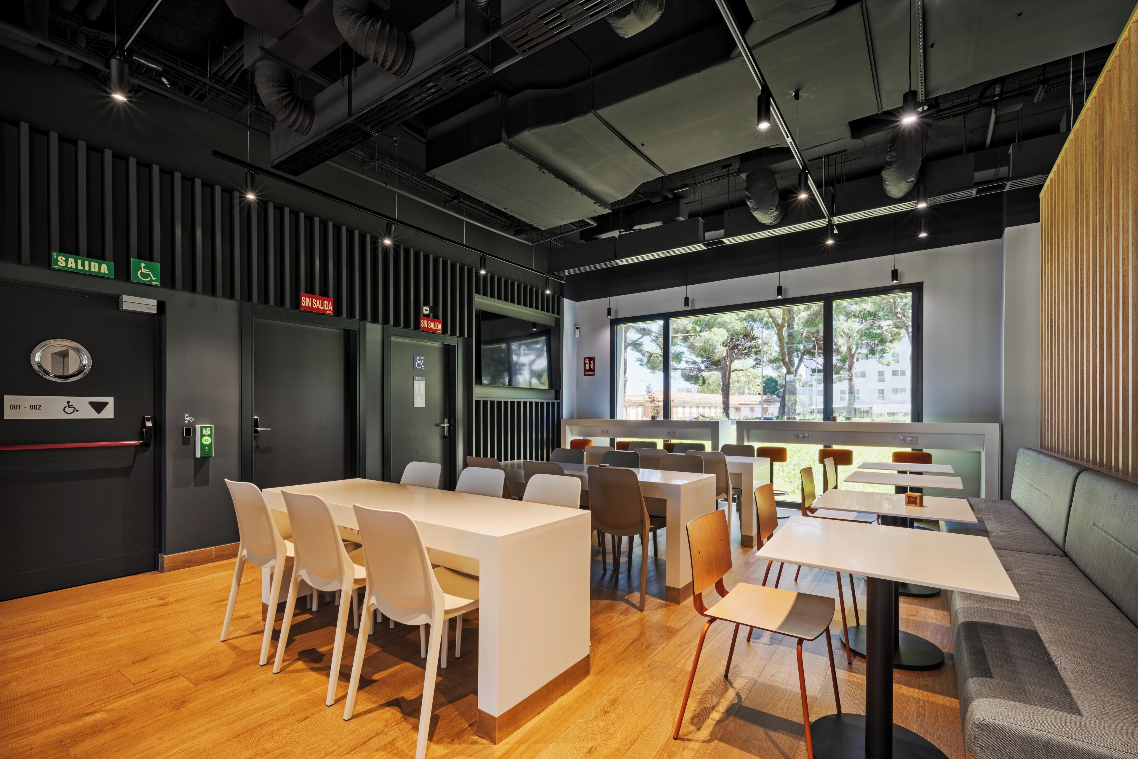 Un área de comedor moderna con mesas, sillas, una barra y vistas al exterior a través de amplias ventanas.