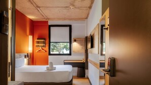 A modern hotel room with a bed, bedside table, lamp, and a view of greenery outside.