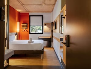 Una habitación de hotel moderna con cama, mesita de noche, lámpara y vistas al exterior con zonas verdes.