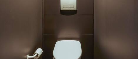 Eine kleine, moderne Toilette mit weißer Toilette, Papierhandtuchspender und einer an der Wand angebrachten Spülung.
