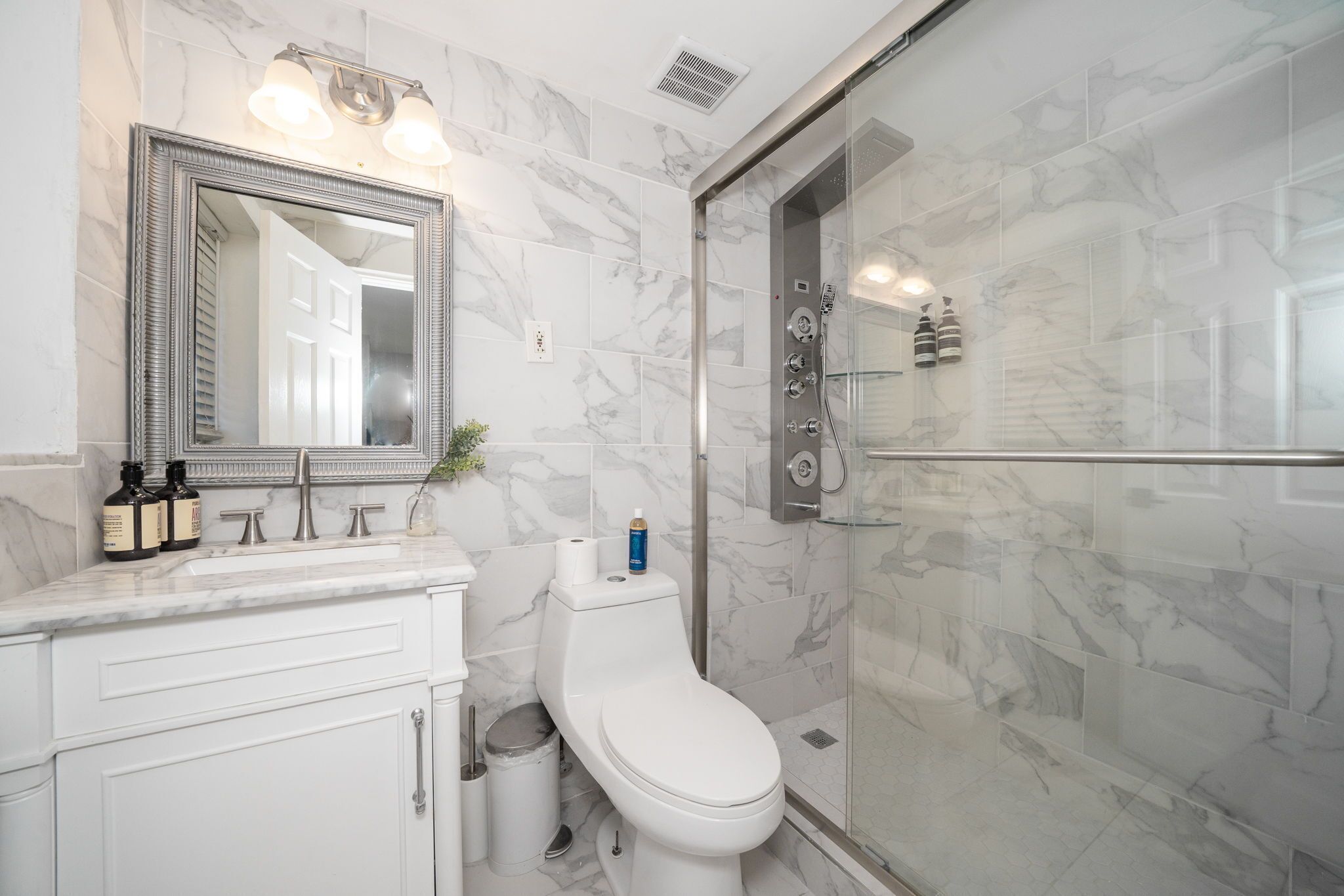 A modern bathroom with a marble backsplash, a large mirror, a glass-enclosed shower, and a white toilet.