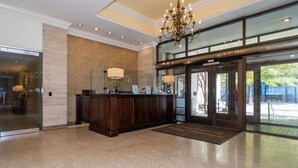 Un espace d’accueil avec un mur en marbre, un comptoir de réception en bois, un lustre et une porte en verre donnant sur l’extérieur.