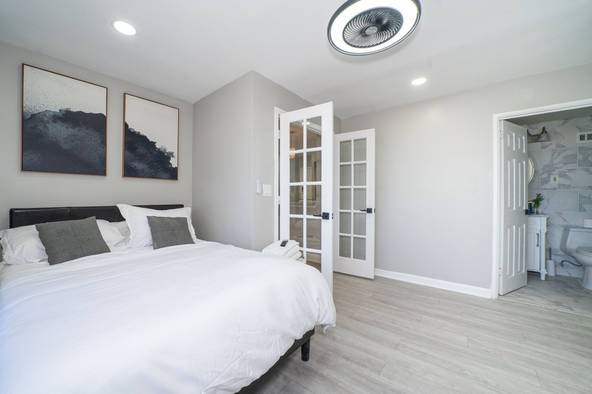A bedroom with a bed, a door leading to a bathroom, and two framed pictures on the wall.