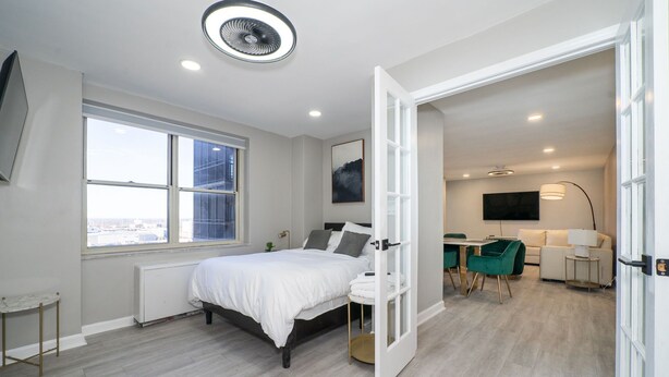 Une chambre moderne avec un grand lit, un bureau et une vue sur la ville grâce à une grande fenêtre.