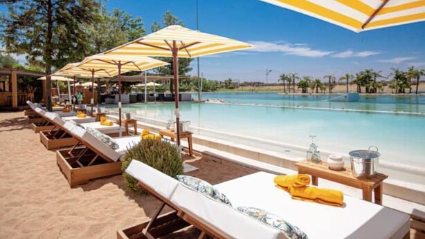 A poolside area with sun loungers and striped umbrellas, a sandy beach, and a clear view of the pool. - Villa Marrakech Piscine Privée vue sur Golf&atlas (Marrakech)