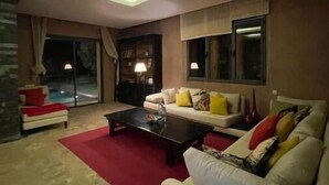 A modern living room with a sofa, a coffee table, and a red rug. There are large windows and a skylight. - Villa Marrakech Piscine Privée vue sur Golf&atlas (Marrakech)