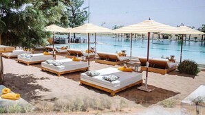 A poolside area with lounge chairs and umbrellas, a wakeboarding area, and a view of the water. - Villa Marrakech Piscine Privée vue sur Golf&atlas (Marrakech)
