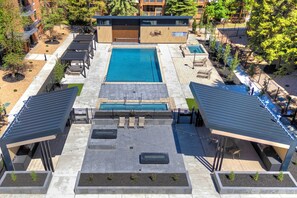 Un área de piscina en la azotea con una piscina grande central, zonas de estar y un patio cubierto.