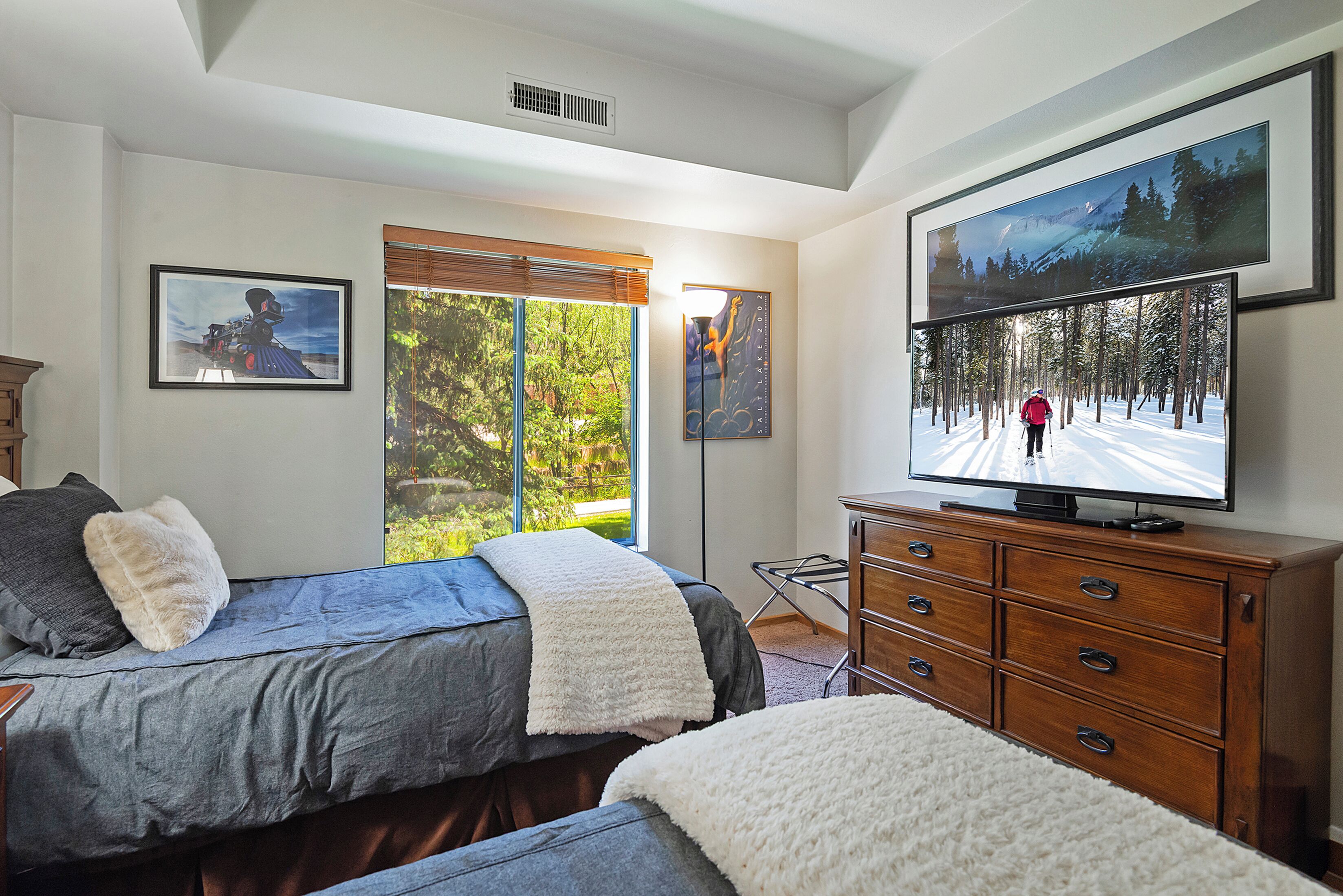 A bedroom with a bed, a dresser, a television, and framed pictures on the wall.