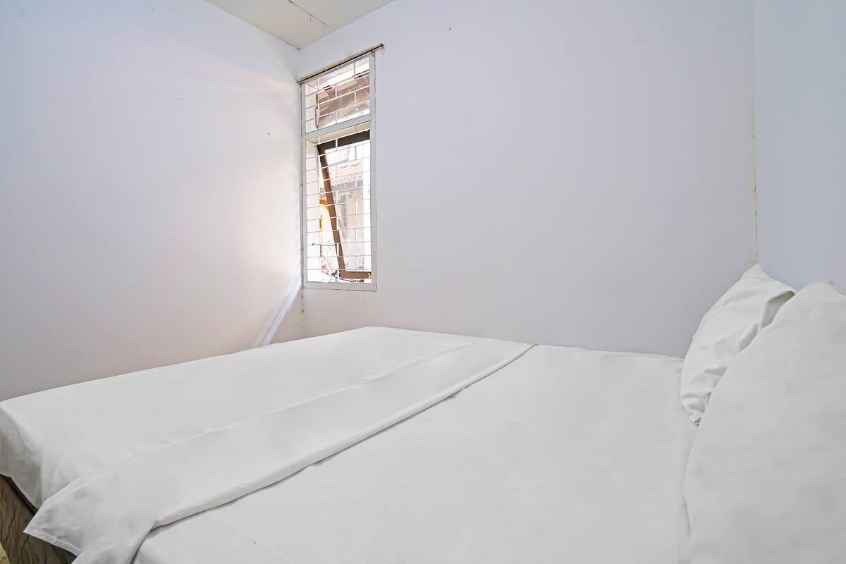 A small, single-bed room with white walls and a window with blinds.